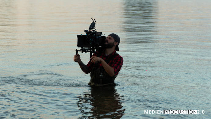 Mann steht mit Filmkamera im Wasser