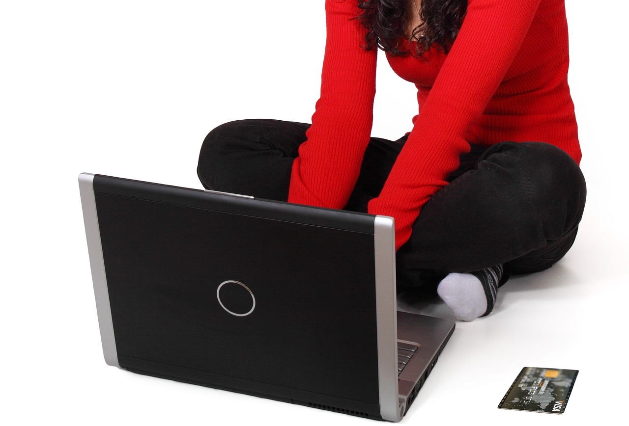 Frau im roten Pulli sitz auf Boden am Laptop und tippt 